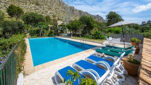 A swimming pool with lounge chairs and a patio area, surrounded by greenery and a mountain backdrop. - Villa Piedra, Surrounded by nature, but close to Port Pollensa (Pollença)