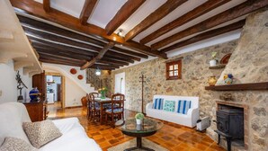A rustic room with exposed wooden beams, a stone wall, a fireplace, and a dining area with a round table and chairs. - Villa Piedra, Surrounded by nature, but close to Port Pollensa (Pollença)