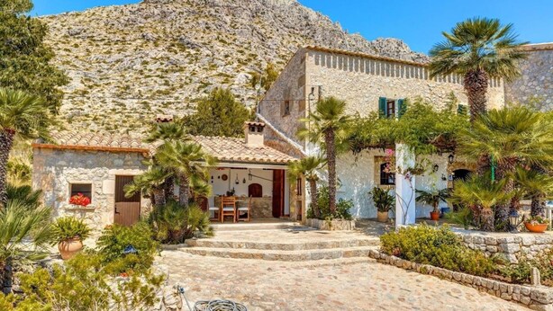 A stone building with a tiled roof, a stone staircase leading to a door, and a garden with potted plants and a palm tree. - Villa Piedra, Surrounded by nature, but close to Port Pollensa (Pollença)