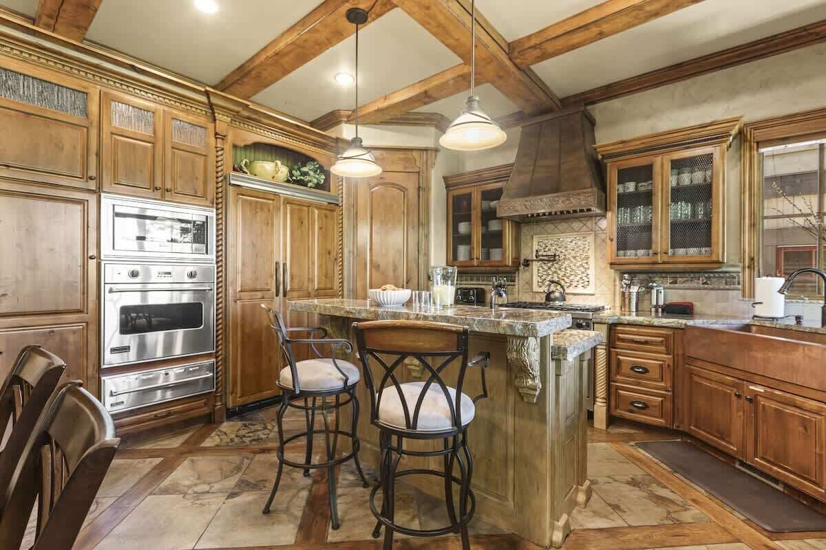 A kitchen with wooden cabinets, a built-in oven, bar stools, and pendant lighting.