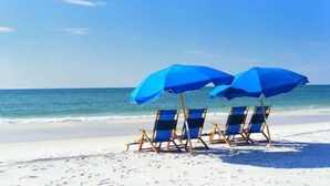 A beach with three blue beach chairs and two blue umbrellas. - Turtles Nest  Mins to the Beach Family Condo (Destin)