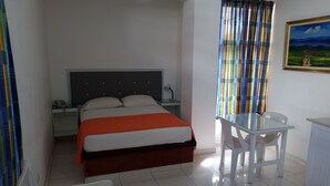 Een hotelkamer met een bed, een bureau, een stoel, een tafeltje, een schilderij en gordijnen.