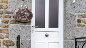 Una puerta blanca con un panel de vidrio esmerilado, una pared de piedra, un letrero colgante y una reja de metal.