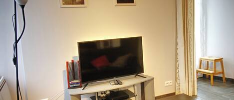 A living room with a flat-screen TV on a stand, a lamp, a small table, and two framed pictures on the wall.