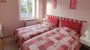 Un dormitorio con dos camas, una ventana, un radiador, una mesita de noche y un ventilador de techo.