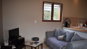 Ein Wohnzimmer mit Fernseher, Sofa, Couchtisch und einem Fenster mit Jalousien.