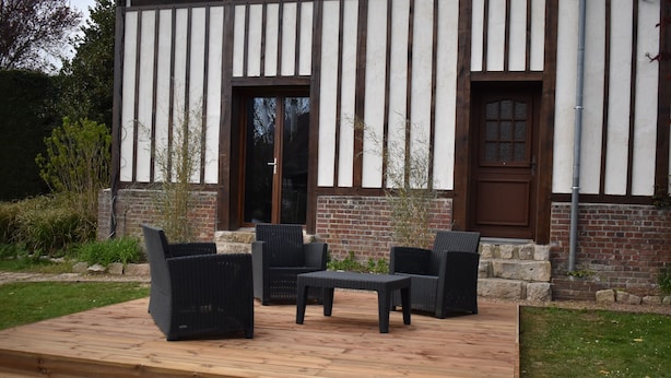 Eine Holzterrasse mit Gartenmöbeln, ein Backsteinhaus mit weiß-brauner Fassade und eine Tür mit Glasverkleidung.