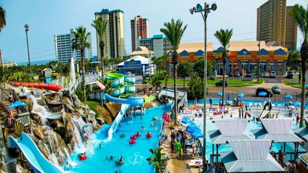 A water park with multiple slides and pools, surrounded by palm trees and urban buildings. - Mermaids Retreat Mins to Beach Family Condo (Destin)