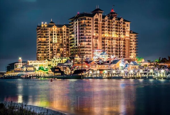 A large hotel with multiple floors and balconies, situated by a waterfront with a dock and boats.