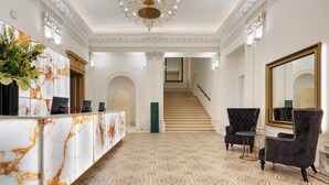A grand lobby with a marble reception desk, a chandelier, a staircase, and classic armchairs. - Aurea Ana Palace by Eurostars Hotel Company (Budapest)