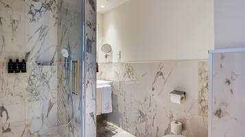 Un baño moderno con ducha de vidrio, paredes de mármol, inodoro y lavamanos con toallero.