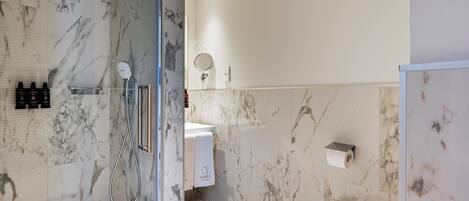 A modern bathroom with a glass-enclosed shower, marble walls, a toilet, and a sink with a towel rack.