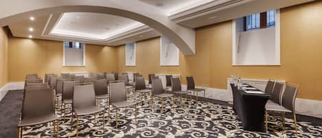 Un salón de conferencias con hileras de sillas, una mesa negra y una alfombra estampada.