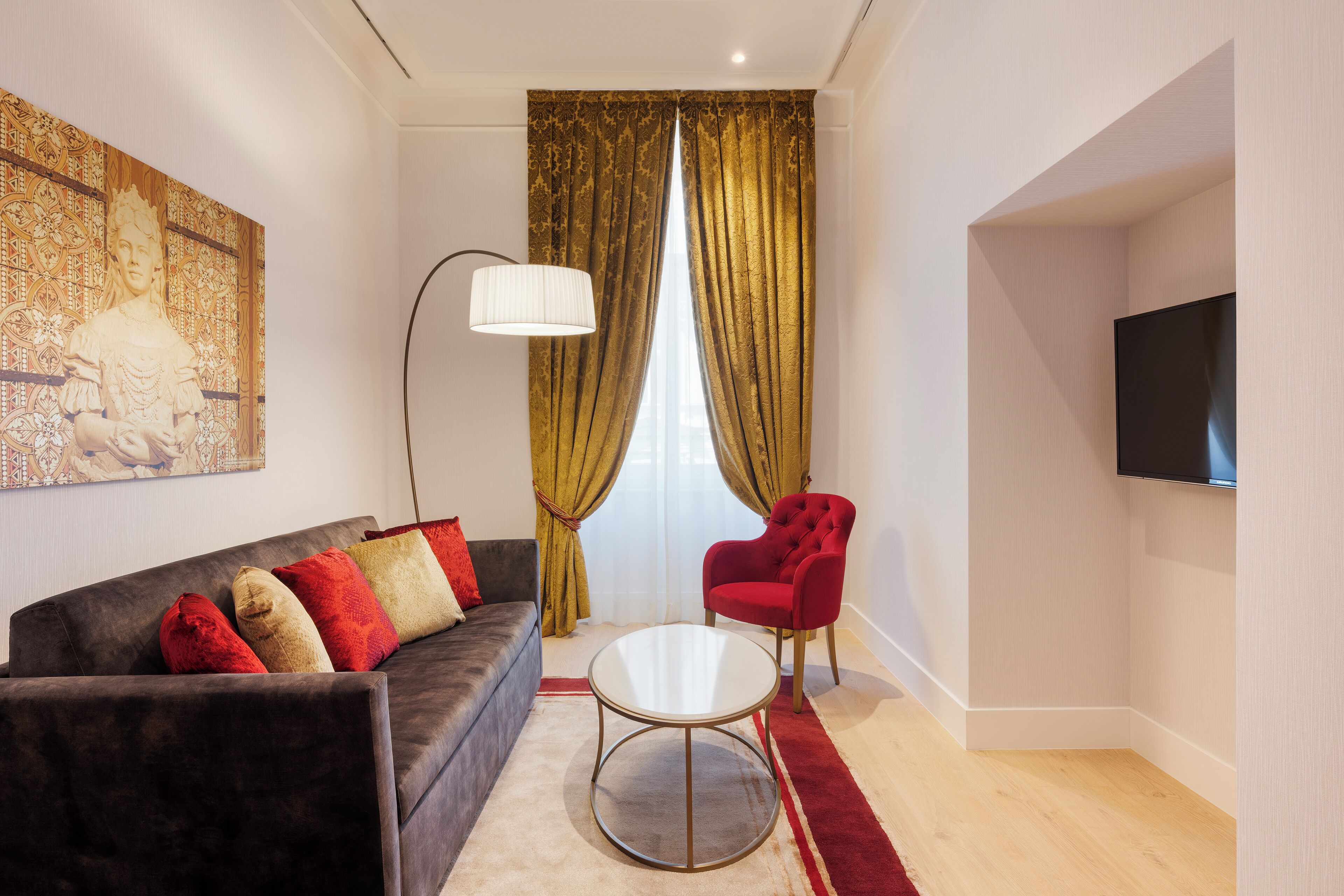 Ein modernes Wohnzimmer mit einem dunklen Sofa, roten und beigen Kissen, einem runden Couchtisch, einem roten Sessel, einer Stehlampe und einem großen Gemälde an der Wand.