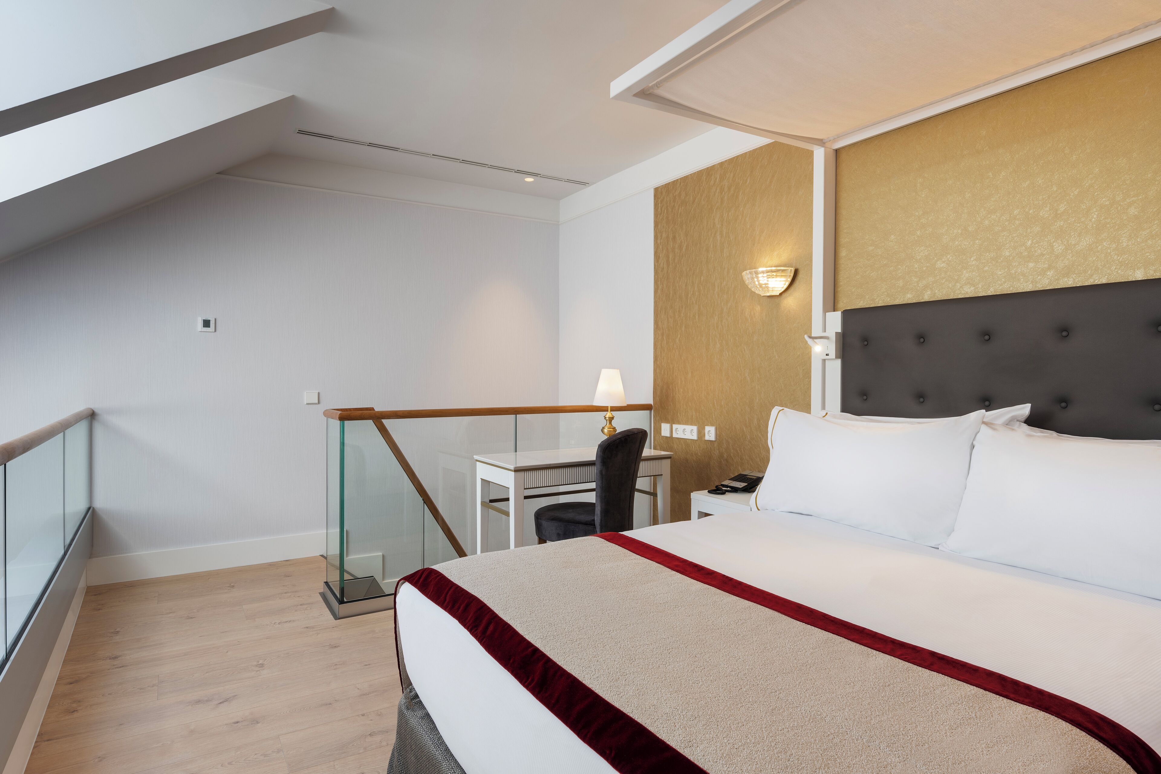 Habitación de hotel con una cama grande, un escritorio, una silla y un balcón con barandilla de vidrio.