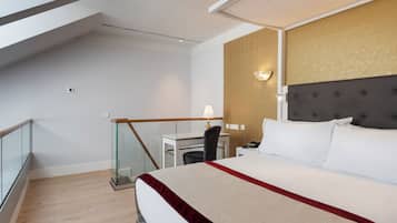 Habitación de hotel con una cama grande, un escritorio, una silla y un balcón con barandilla de vidrio.