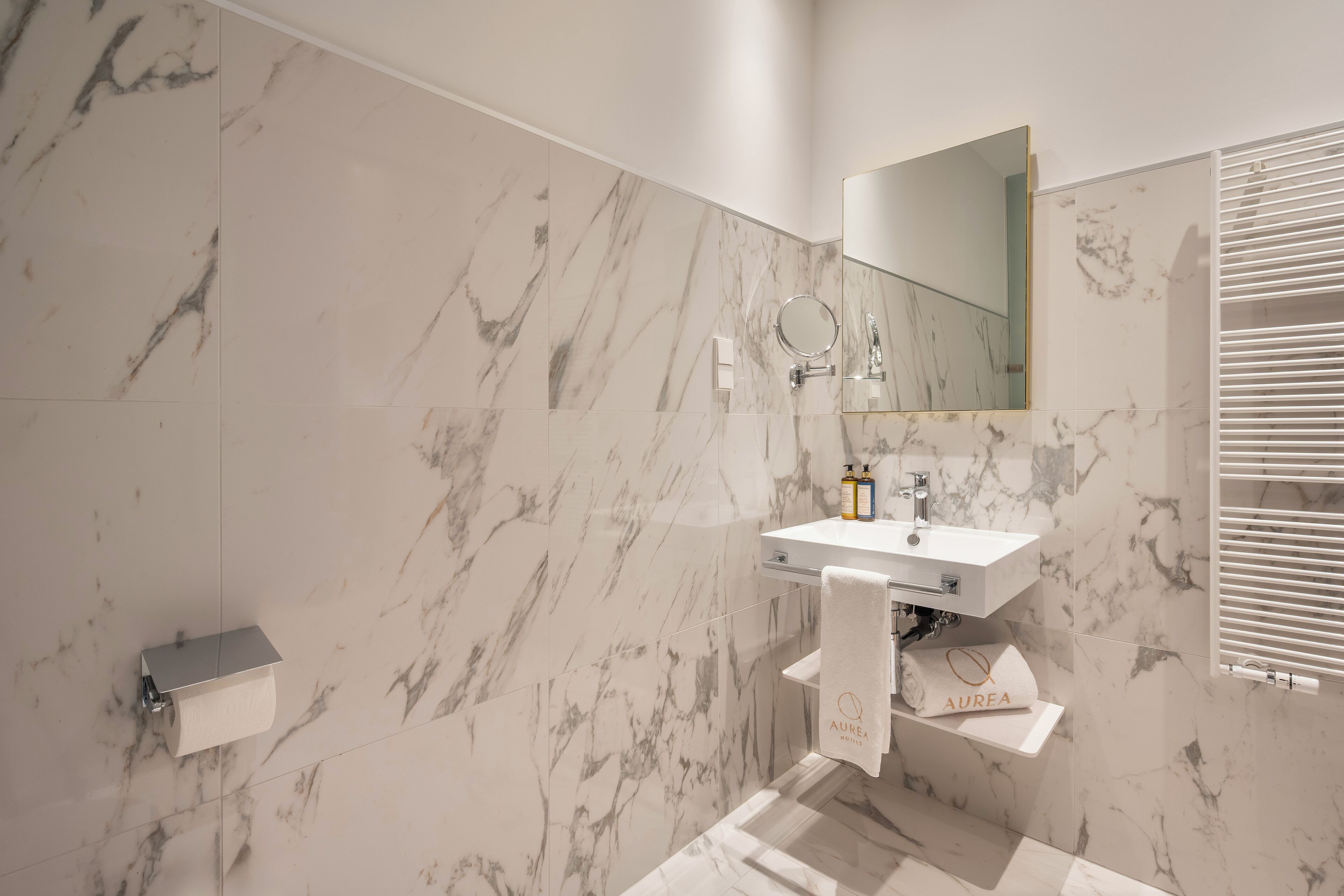 A bathroom with a marble wall, a sink with a mirror, and a towel rack.