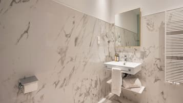 A bathroom with a marble wall, a sink with a mirror, and a towel rack.