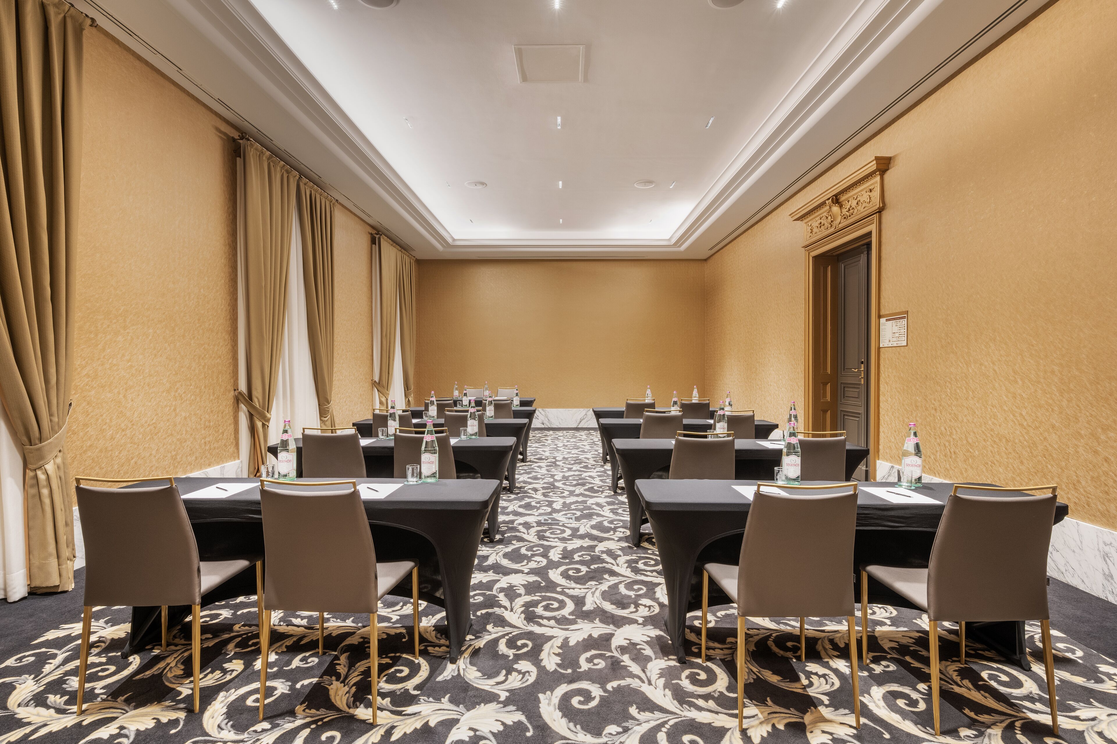 A conference room with tables and chairs, a patterned carpet, and a ceiling with recessed lighting.