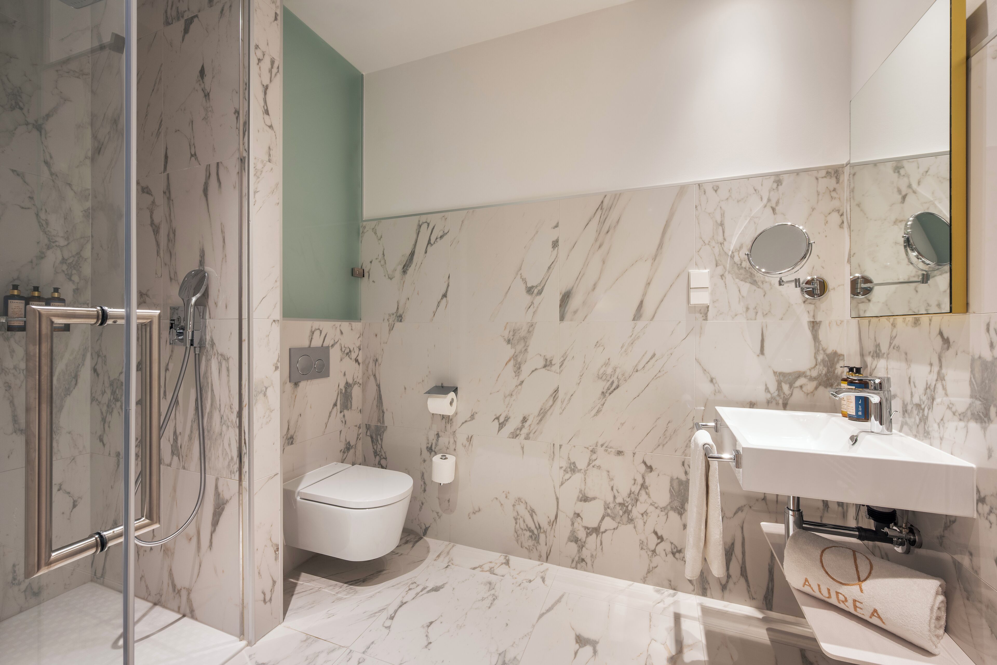 A modern bathroom with a marble floor, a white toilet, a glass-enclosed shower, and a sink with a mirror above it.