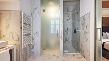 Un baño moderno con ducha de vidrio, paredes de mármol y un lavamanos blanco.