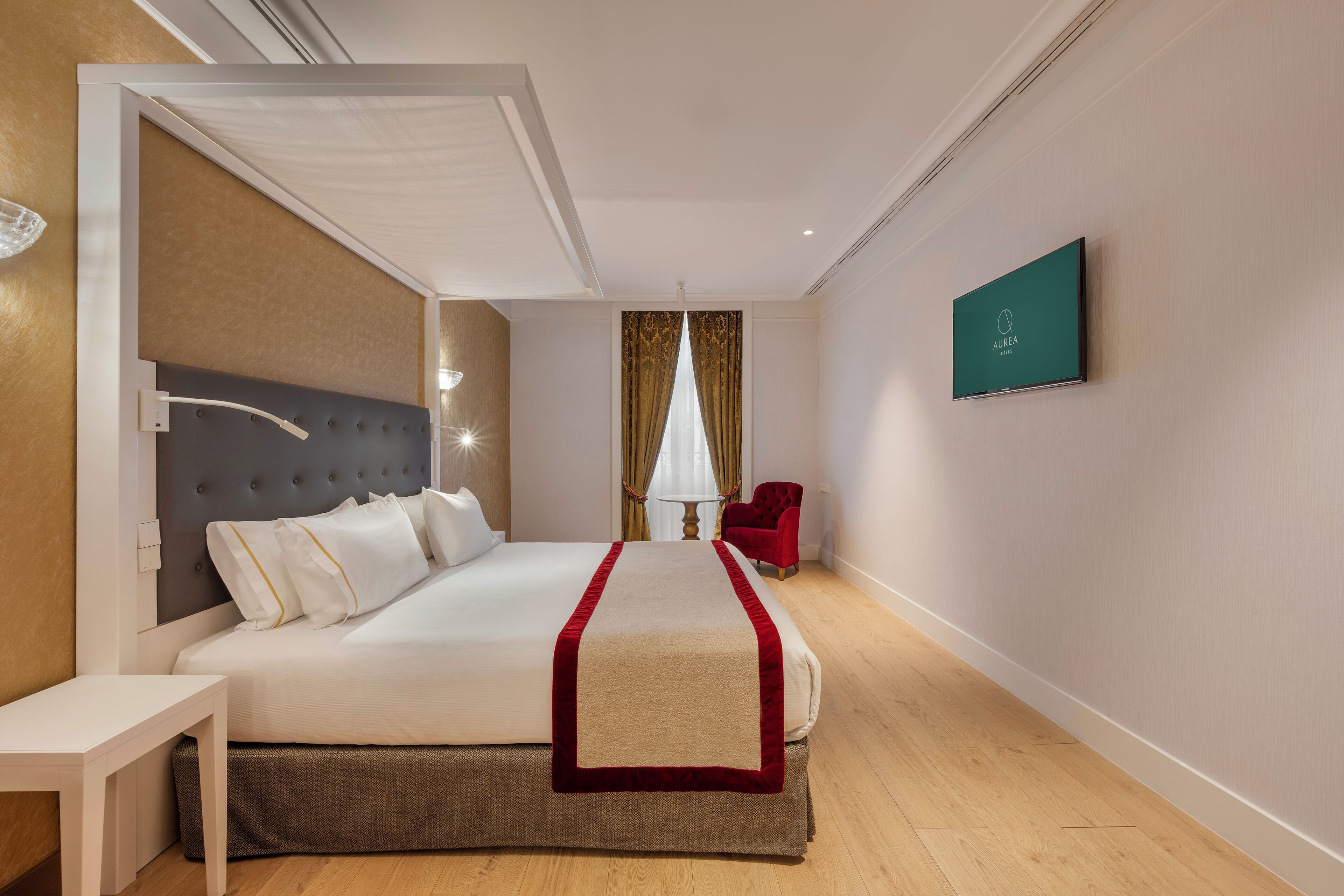 Habitación de hotel con una cama grande, una mesita de noche, una silla roja, un televisor y una ventana con cortinas.