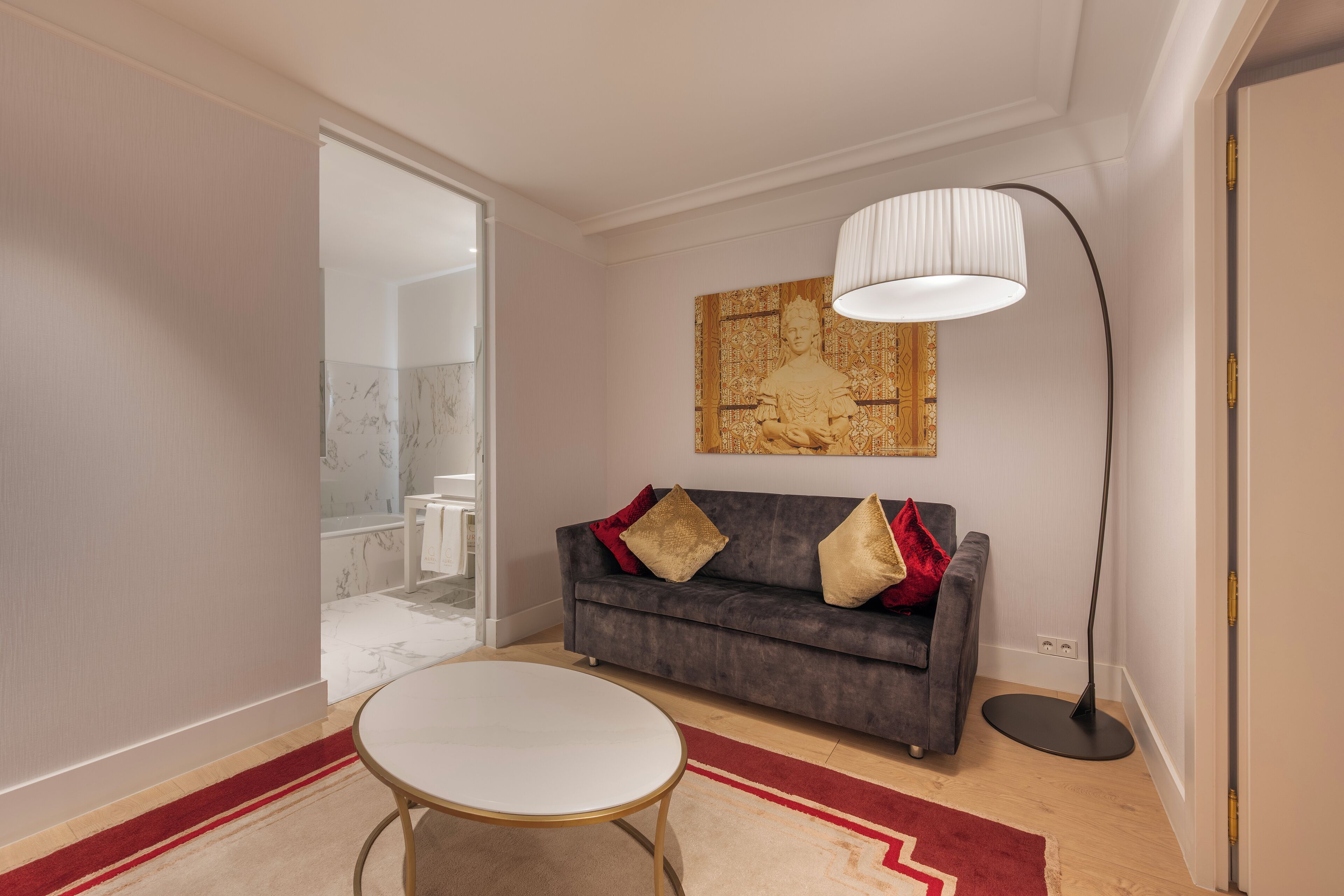 A modern living room with a grey sofa, a round coffee table, a floor lamp, and a red and beige rug.