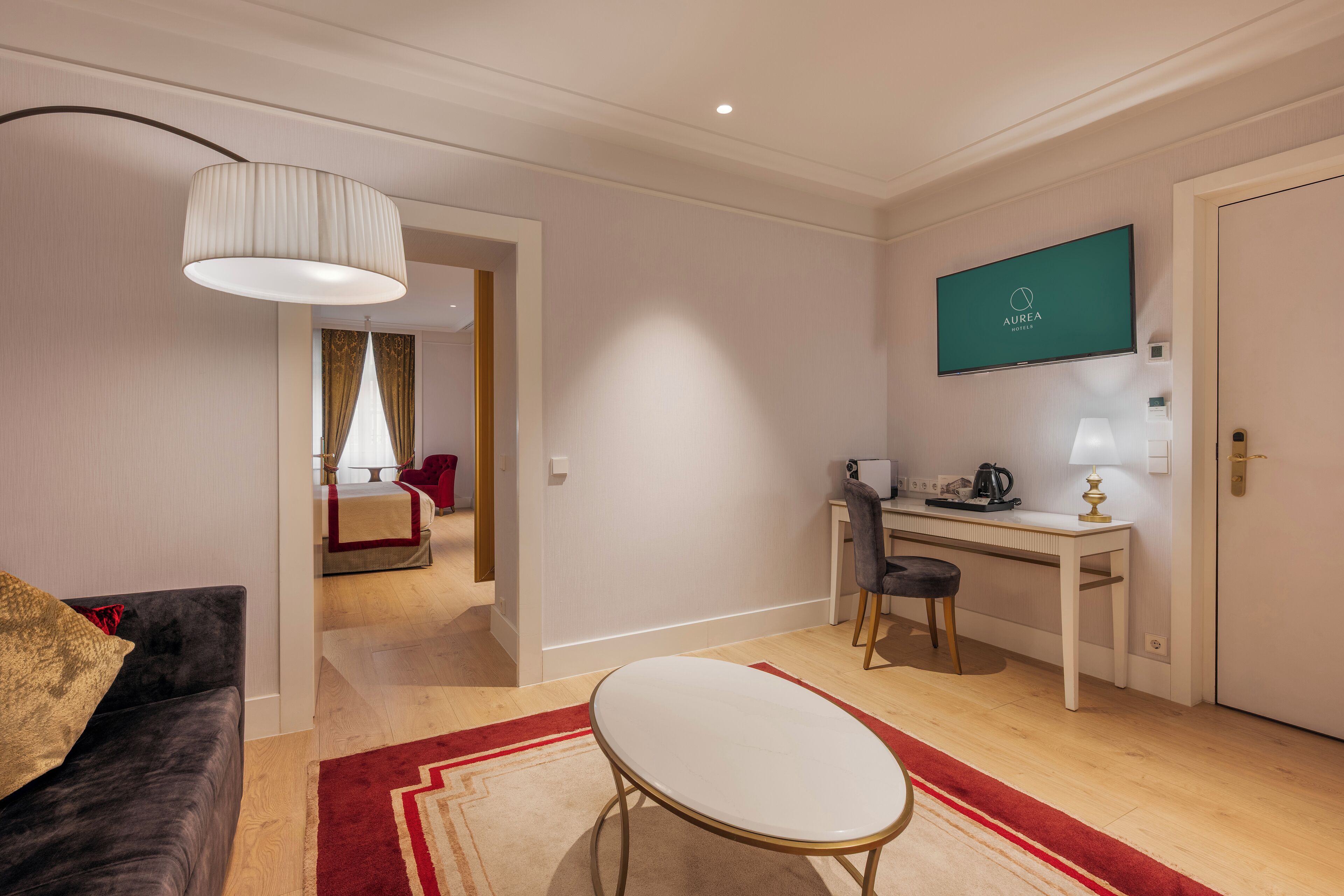 Una habitación de hotel moderna con comedor, televisor montado en la pared y una sala de estar separada con sofá y lámpara.