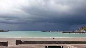 Une plage avec un mur de pierres, un phare et des bateaux sur l’eau.