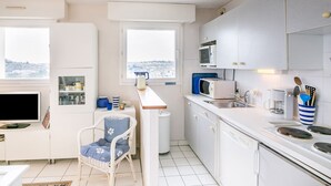 A compact kitchen with white cabinets, a microwave, a coffee maker, and a window with a view of the city. - La Lagune - Appartement vue mer (Pléneuf-Val-André)