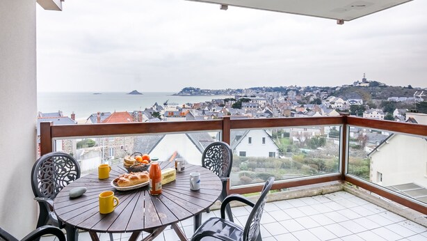 A balcony with a table set for breakfast, overlooking a coastal cityscape. - La Lagune - Appartement vue mer (Pléneuf-Val-André)
