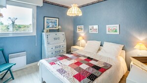 A bedroom with a bed, a dresser, a nightstand, a lamp, and a window with a view. - La Lagune - Appartement vue mer (Pléneuf-Val-André)