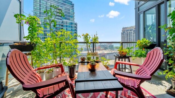 A balcony with two red Adirondack chairs, a wooden table, and potted plants.