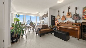 A spacious living room with a piano, multiple guitars, and a dining area with a view.