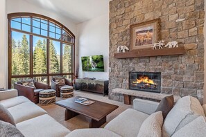 A living room with a stone fireplace, large windows, and a cozy seating area. - Base Camp 490 Private Hot Tub (Winter Park)
