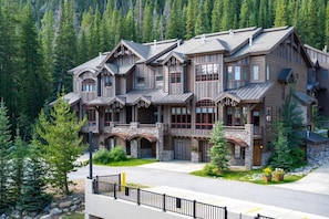 A multi-story lodge with a stone facade, multiple balconies, and a forest backdrop.