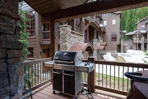 A covered outdoor area with a grill, stone pillars, and a view of a multi-story building.