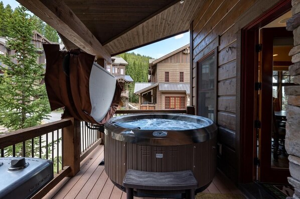 A wooden deck with a hot tub, a covered area, and a view of surrounding buildings.