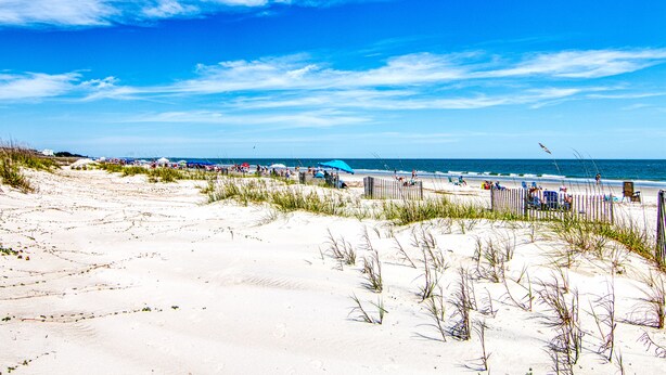 A beach with sand dunes, a wooden fence, and a clear blue sky.