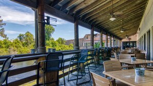 An outdoor patio with wooden tables and chairs, a view of the surrounding greenery, and a covered area with a wooden ceiling.