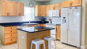 A modern kitchen with wooden cabinets, a central island with stools, a refrigerator, and a microwave.