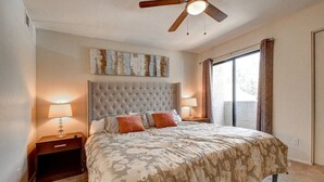Een slaapkamer met een gestoffeerd hoofdeinde, twee bedlampen, een groot raam met gordijnen en een plafondventilator.