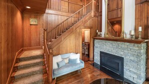 A wooden staircase leading to a second floor, a stone fireplace, and a blue sofa in a room with wooden paneling. - Breakwater Estate… perfect for Large Group Getaways! (Mattituck)