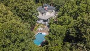 A large house surrounded by dense forest, with a swimming pool and outdoor seating area. - Breakwater Estate… perfect for Large Group Getaways! (Mattituck)
