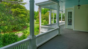 A covered porch with white railings and columns, overlooking a well-maintained garden and a road. - Breakwater Estate… perfect for Large Group Getaways! (Mattituck)