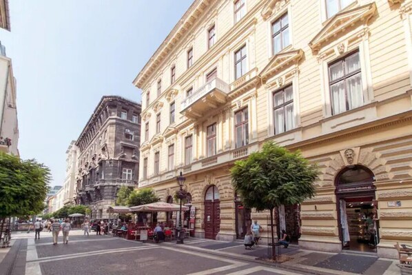 Una calle con edificios históricos, mesas al aire libre en cafés y peatones.