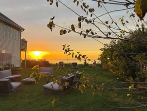 Un jardin avec une terrasse, une maison et une vue sur le coucher de soleil.