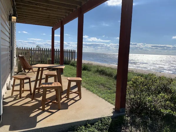 Un porche cubierto con una mesa y sillas de madera, con vista a una playa.