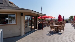 An outdoor dining area with wooden tables and red umbrellas, a clear sky, and a flag on the building. - Balcony overlooks BEAUTIFUL OCEAN VIEW, just steps away from sand! (Hilton Head Island)