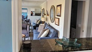 A living room with a sofa, a coffee table, and a kitchen area visible through an open doorway. - Balcony overlooks BEAUTIFUL OCEAN VIEW, just steps away from sand! (Hilton Head Island)